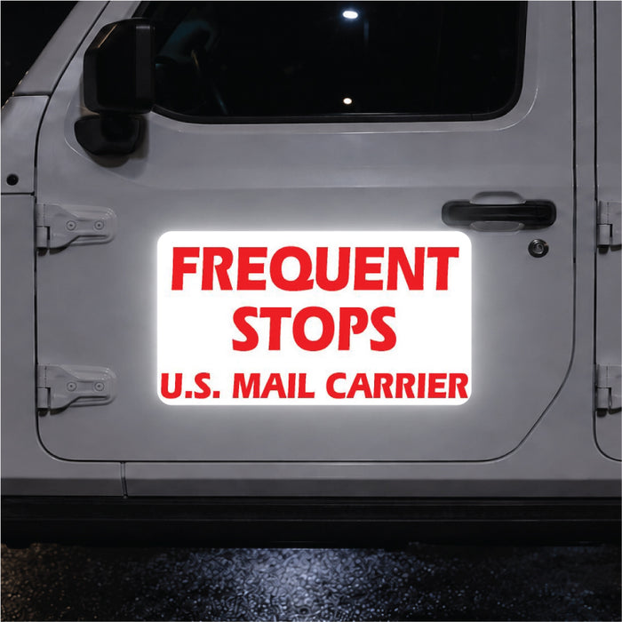 Reflective sign on a vehicle door reading 'Frequent Stops U.S. Mail Carrier' in red text on a white background.