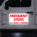 Reflective sign on a vehicle door reading 'Frequent Stops U.S. Mail Carrier' in red text on a white background.