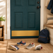 A navy blue entryway door with a wide gold magnetic kickplate, shown in a styled home entryway with a woven rug, shoes, a backpack, and a bench.