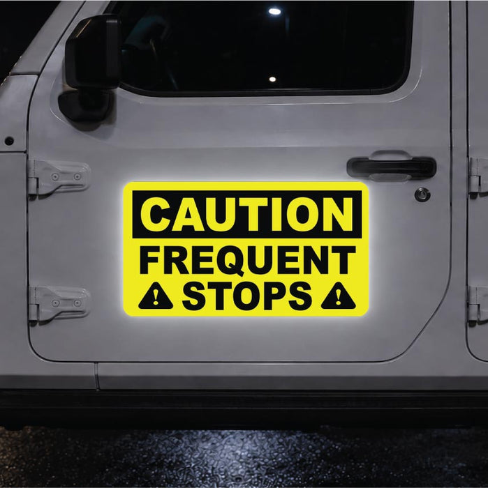 Yellow caution sign on a vehicle door indicating 'Frequent Stops' at night.